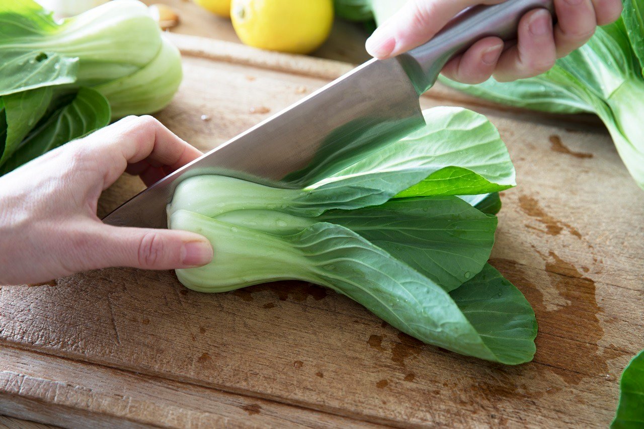 Slicing boy choi in half with chef's knife on cutting board.