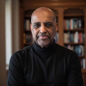 African American male in a library wearing a dark jacket over a turtleneck sweater