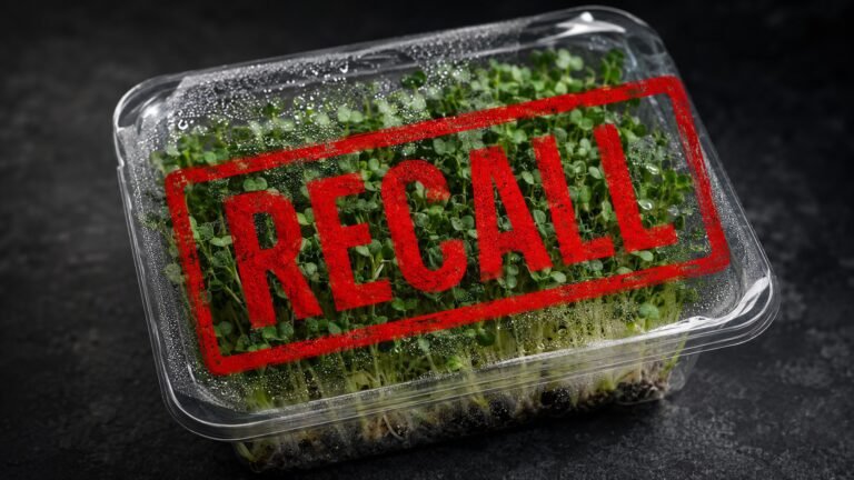 Retail package of fresh broccoli microgreens with a bold red recall stamp overlaid, dark dramatic background